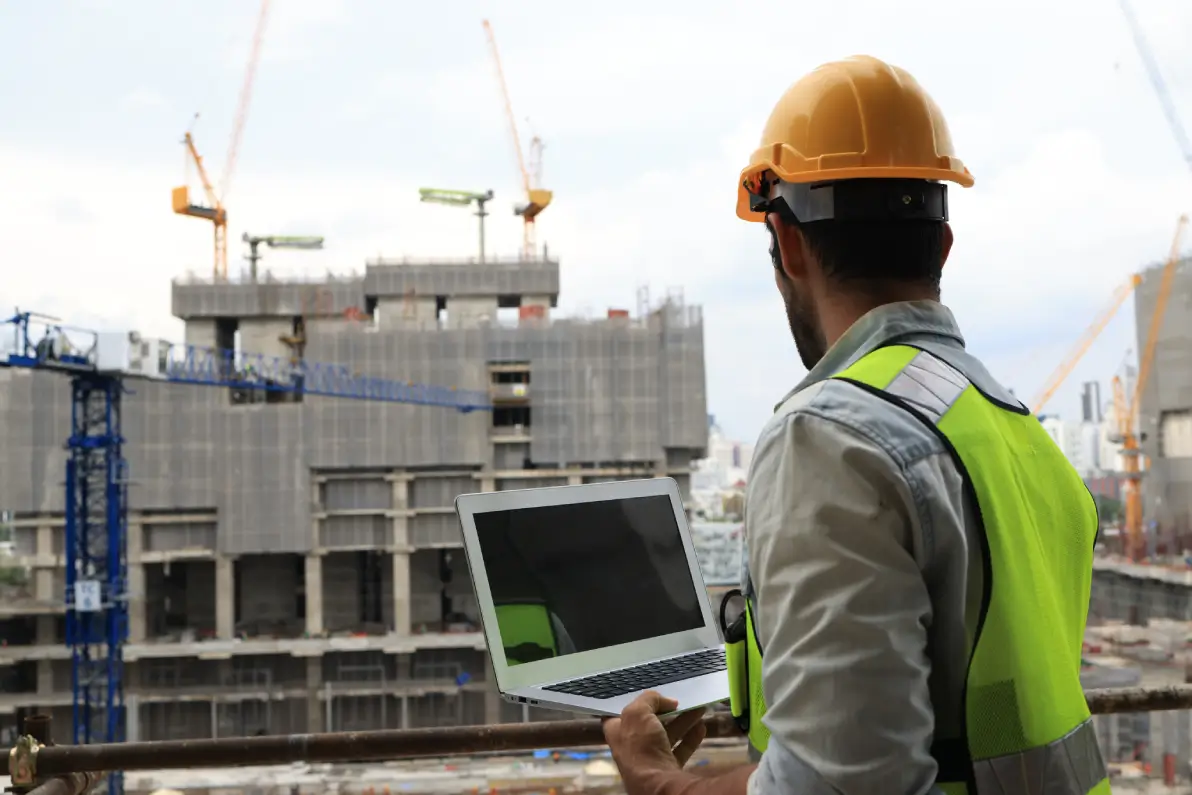 GettyImages-2118046578 (1) Construction worker looking at laptop on site.